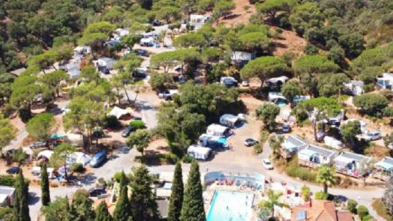 Vista aerea di un campeggio glamping circondato da alberi, con tende, roulotte e camper lungo strade tortuose. In primo piano si vede una piscina, dove le persone si godono il sole: un'opportunità di investimento ideale. 0121Management – ​​l'agenzia di intermediazione per campeggi e immobili per vacanze  