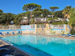 Ein klarer blauer Swimmingpool mit Liegestühlen drum herum, eingezäunt und umgeben von Bäumen und Hütten an einem sonnigen Tag - eine einladende Szene für diejenigen, die investieren oder einen Campingplatz kaufen wollen. 0121Management - der Campingplatz und Ferienimmobilien Makler