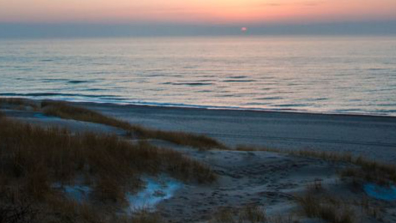 Tramonto sul mare calmo, con vista sulle dune sabbiose punteggiate di erba rada: uno scenario di spiaggia pacifica e tranquilla che invita al relax o a valutare l'investimento in una proprietà per le vacanze per trovare il proprio angolo di paradiso. 0121Management – ​​l'agenzia immobiliare per campeggi e proprietà per le vacanze 